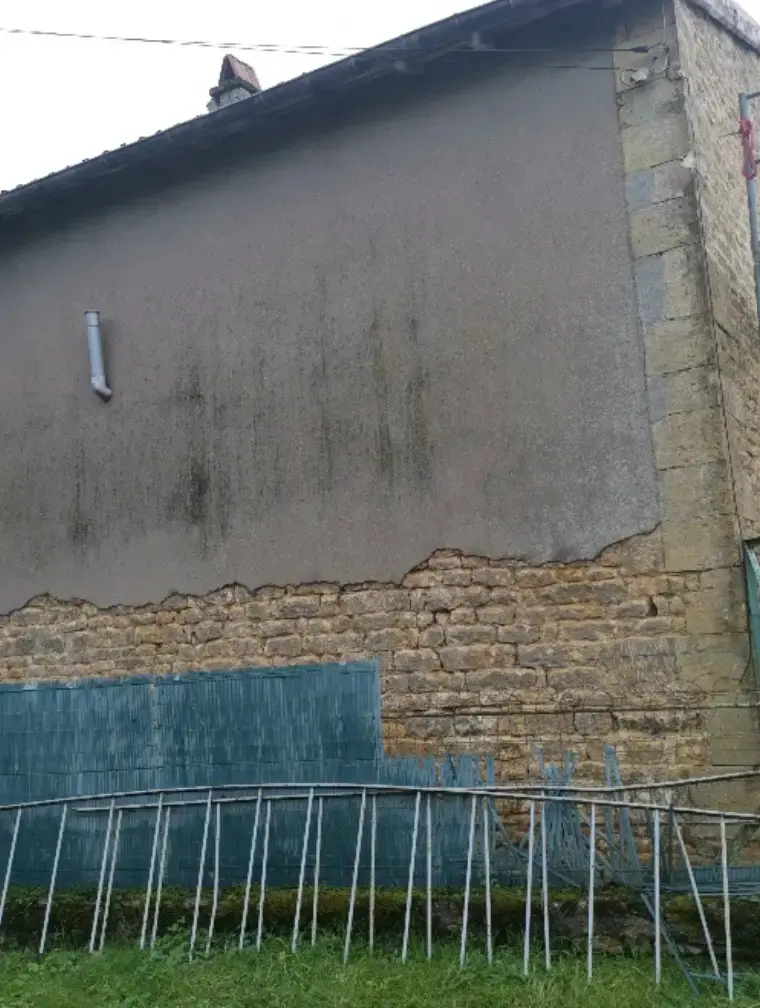 Enduit ciment décollé au pied d'un mur ancien en pierre