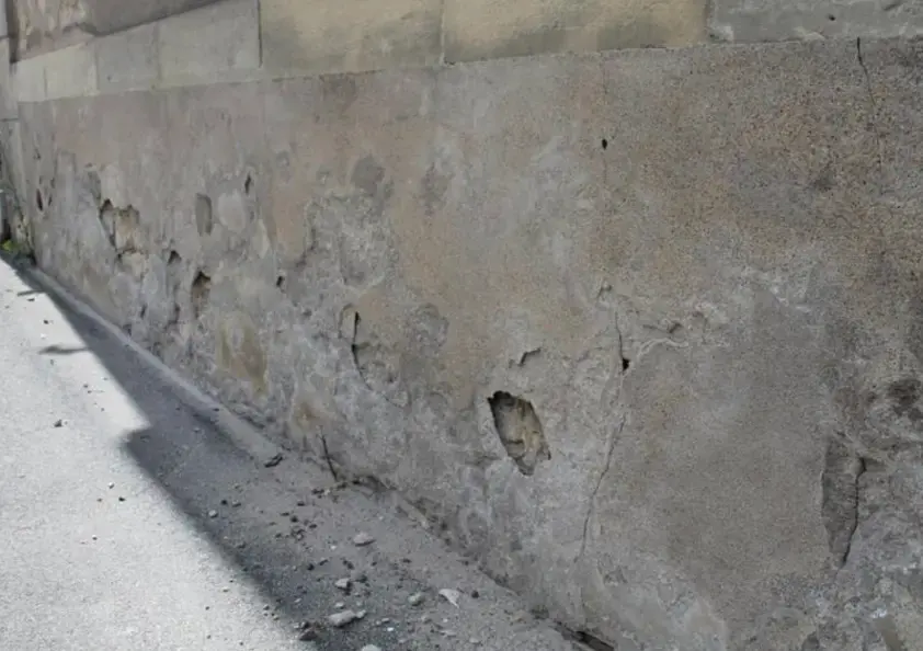 Enduit ciment fissuré et dégradé sur le soubassement d'un mur ancien
