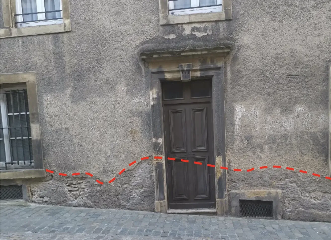 Zone de remontées d'humidité tracée au bas d'une façade ancienne